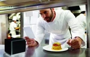 Thermal POS Receipt Printers: Cloud, WiFi, Ethernet & USB 64 Chef in modern, professional kitchen looking at ticket from mC-Print3 thermal receipt and restaurant printer by Star Micronics.